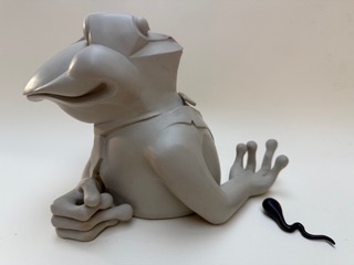 Amphibien à deux têtes Une figurine de grenouille grise, avec une petite créature noire à côté.