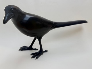 Pie Noire Un oiseau en sculpture noire, debout sur ses pattes, avec un long bec.