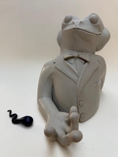 Amphibien à deux têtes Une grenouille en argile portant un smoking, accompagnée d'un petit serpent noir.