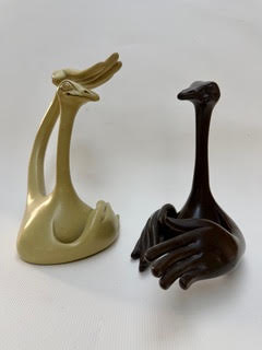 Autruches discutant Deux sculptures stylisées de créatures avec de longs cous, l'une beige et l'autre noire.