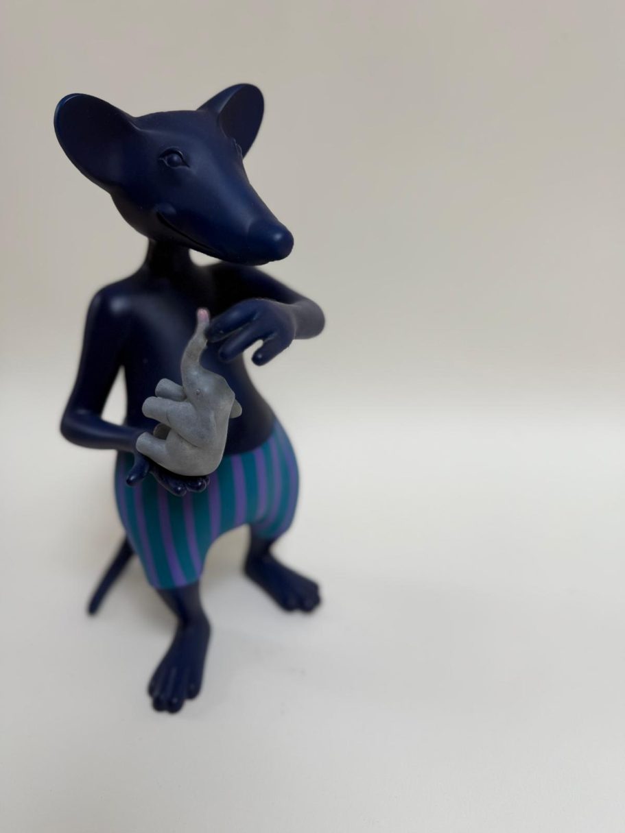 La souris et l'éléphant Souris stylisée debout, corps bleu et rayures vertes, tenant un objet dans ses pattes.