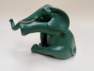 Éléphant vert Éléphant en plastique vert, assis avec une trompe levée et des pattes repliées.