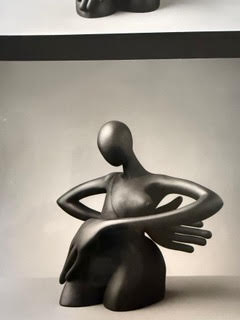Dame 1 Sculpture en métal représentant une figure stylisée assise avec des bras étendus.