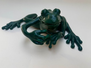 Grenouille Verte Grenouille verte en plastique, posée sur une surface claire, avec les pattes étendues.