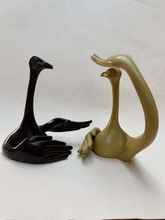Autruches discutant Deux sculptures stylisées en forme de cygnes, l'une noire et l'autre beige.